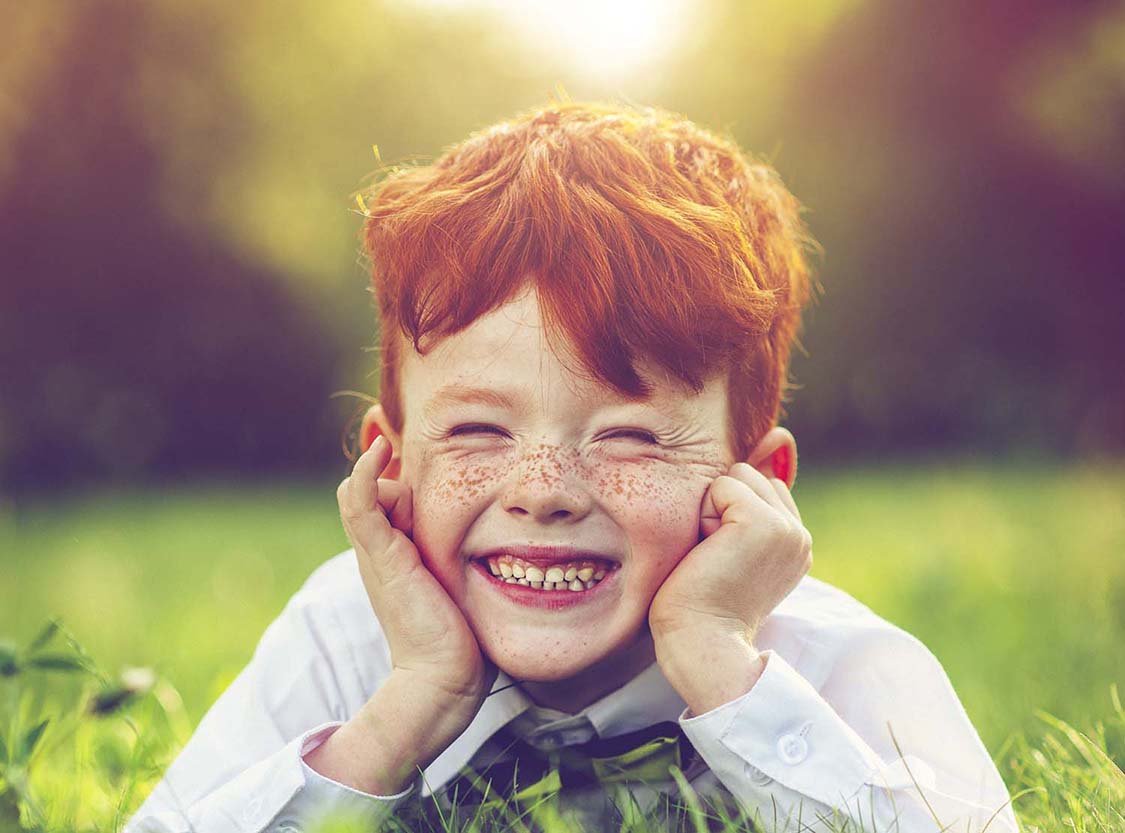Happy child with red hair and freckles in park in summer